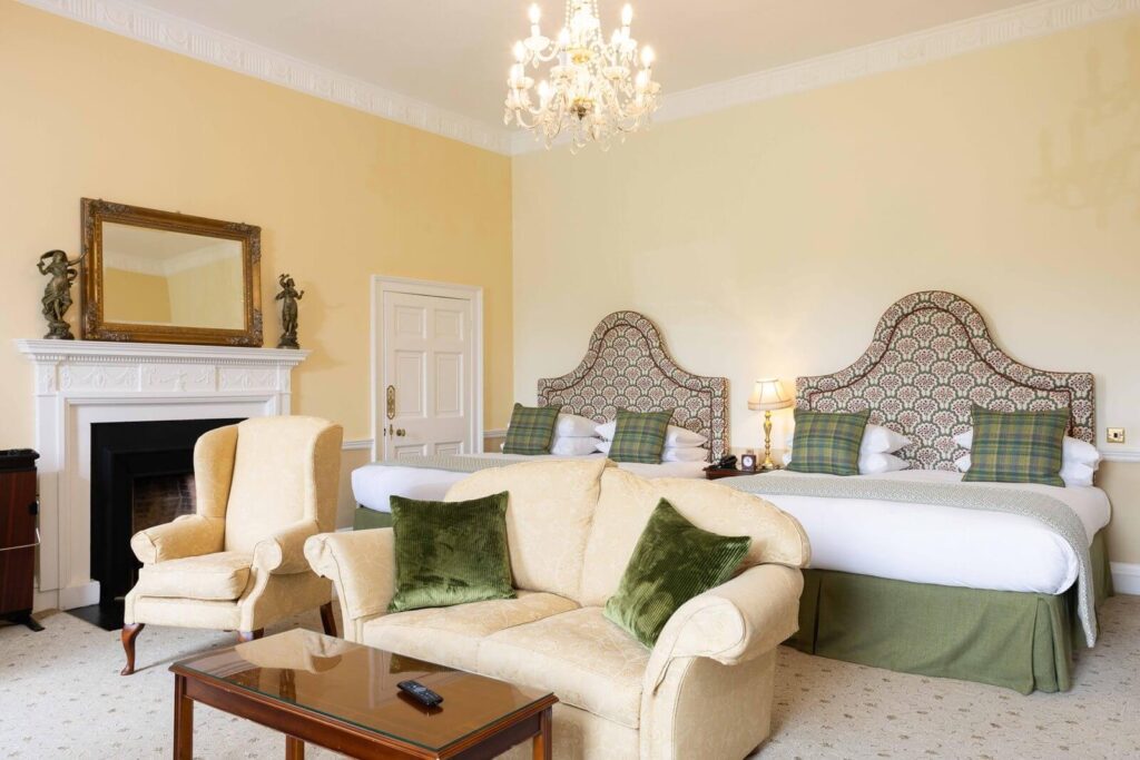 Elegant guest room at Culloden House with two beds, seating area, fireplace and chandelier.